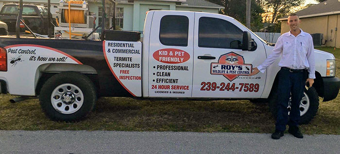 Roy's Wildlife and Pest Control branded pickup truck with a technician standing beside it