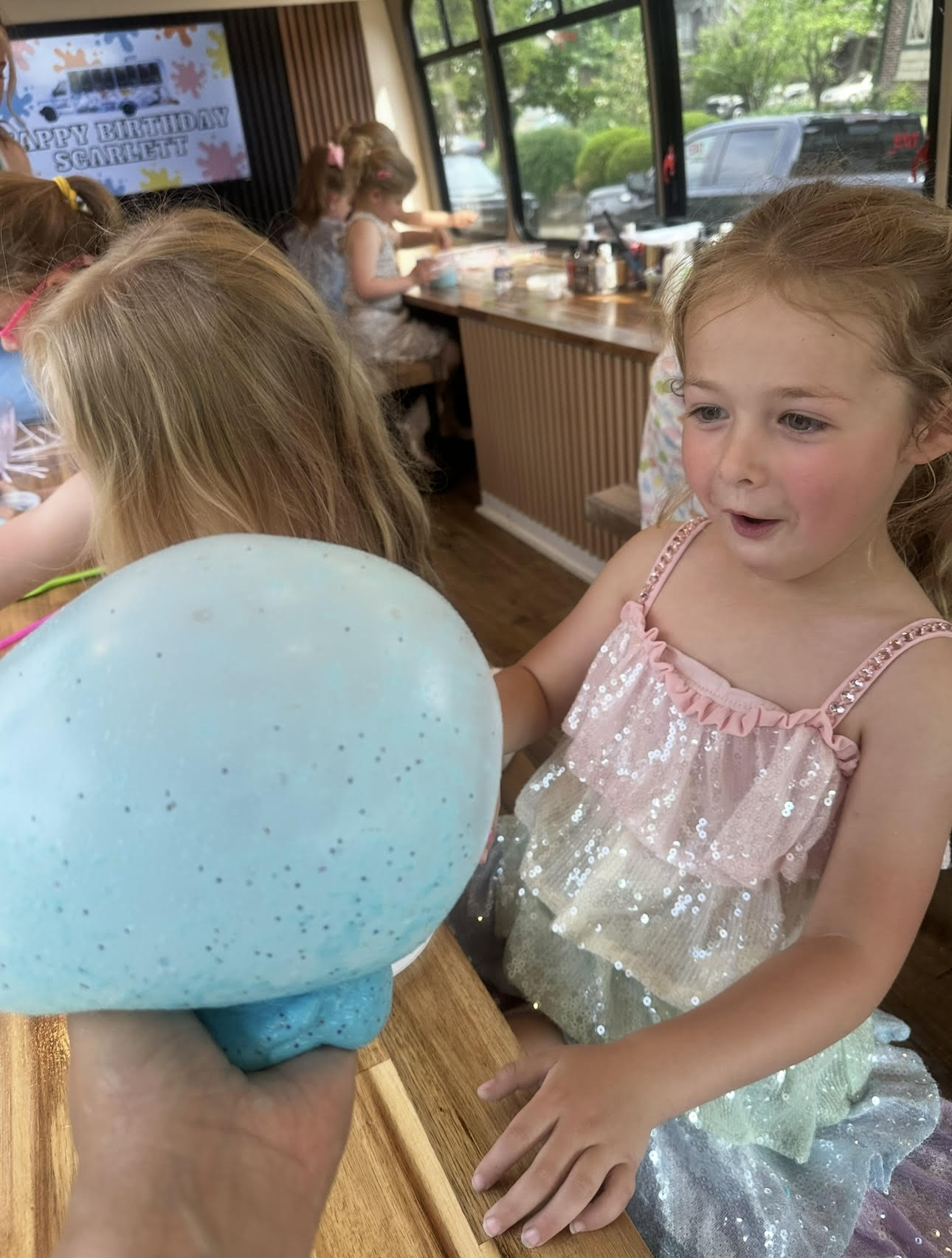 A girl holding a giant blue glitter slime bubble at a birthday party on the bus