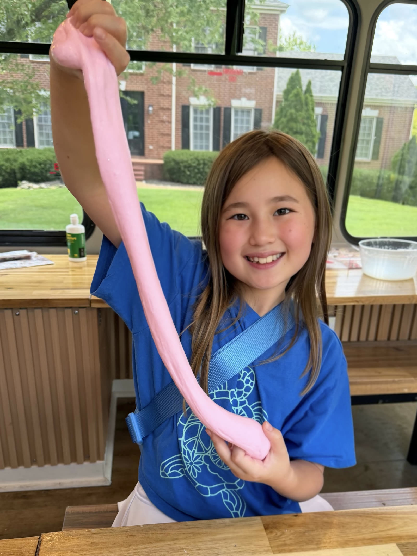 A smiling girl stretching her long pink slime inside the mobile studio bus