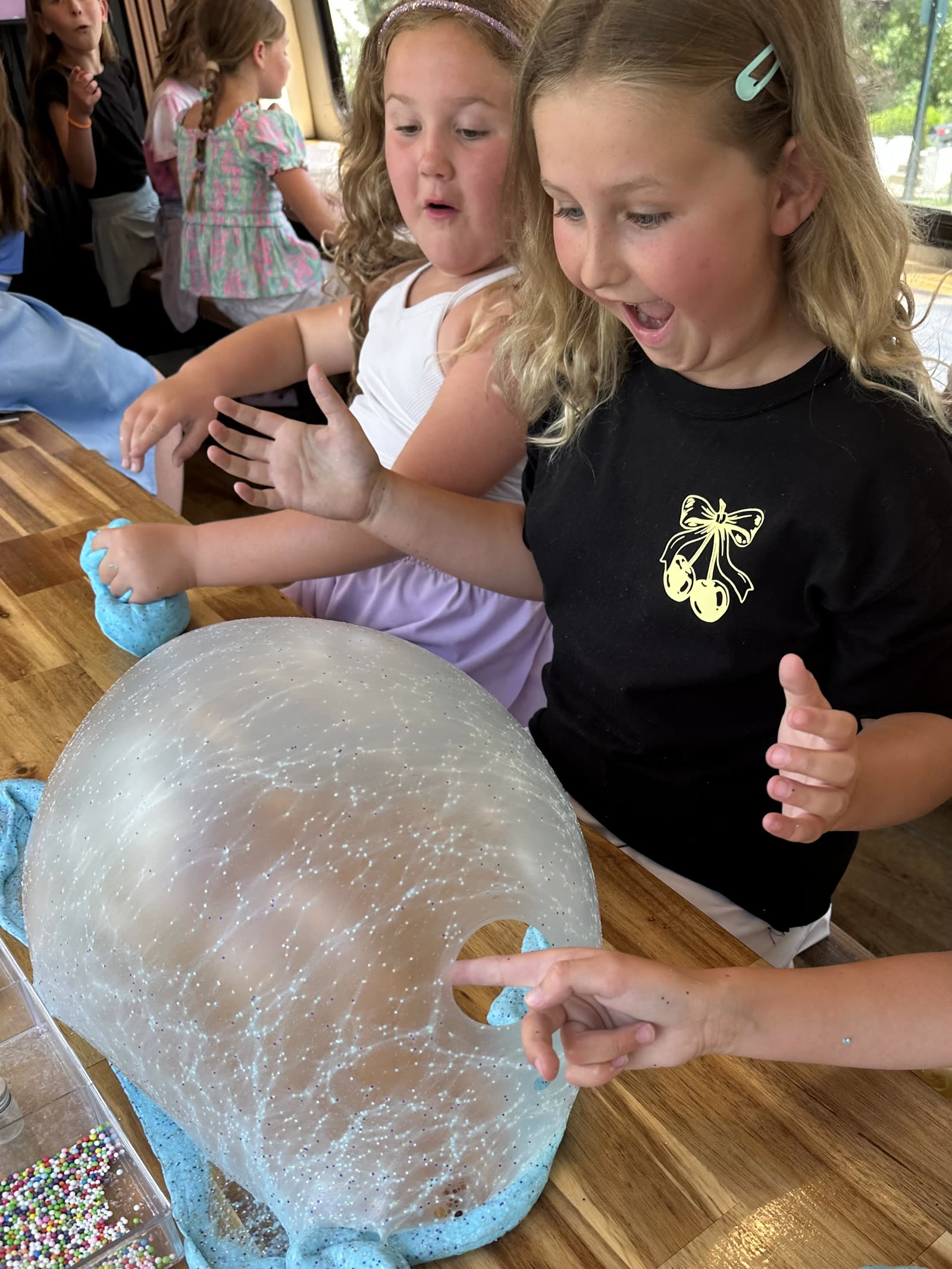 Two girls wide-eyed as they pop a huge glitter slime bubble on the bus