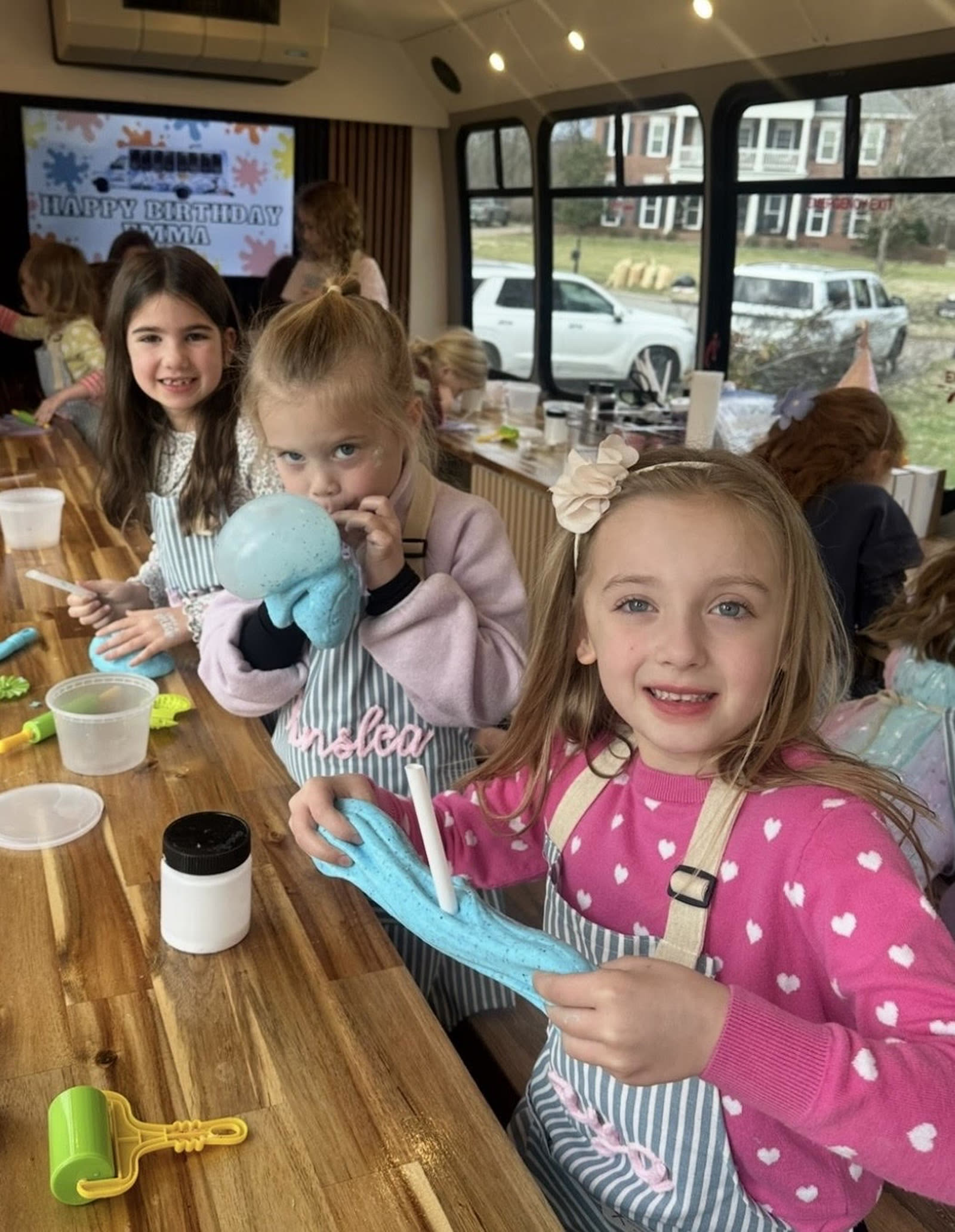 Girls stretching their blue slime at the party table inside the mobile studio bus