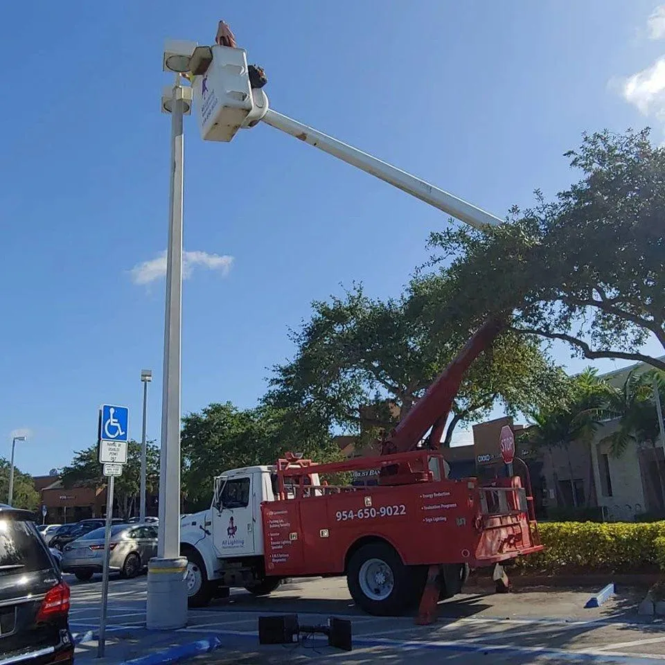 All Lighting Maintenance bucket truck performing an installation or repair on a tall commercial light pole in a shopping center parking lot.