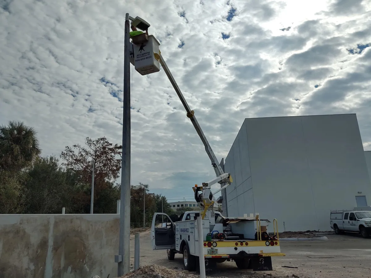 All Lighting Maintenance bucket truck extended to service a tall parking lot light pole at a Florida business complex.