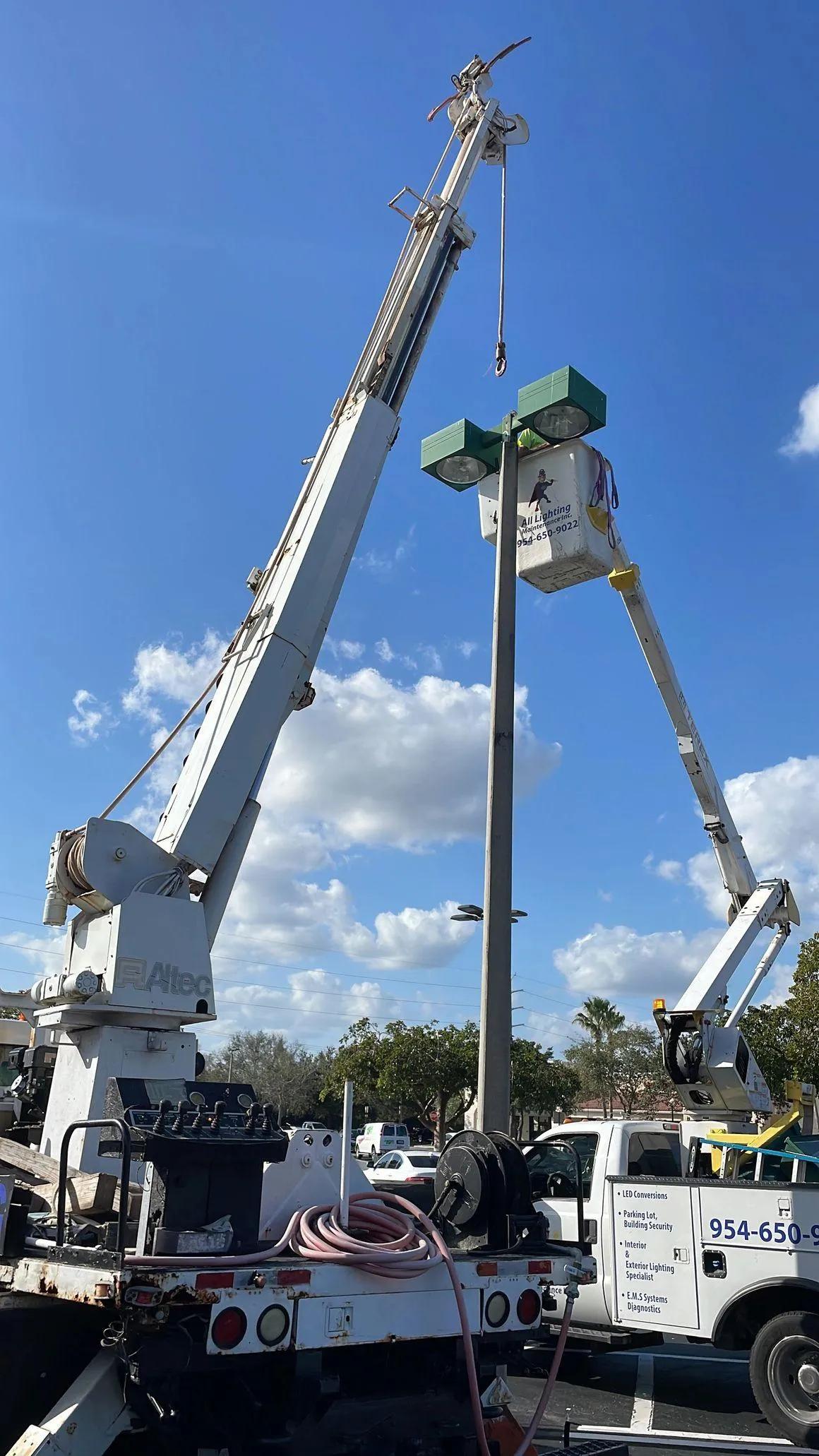 All Lighting Maintenance crane truck and bucket truck performing a heavy-duty parking lot light pole repair in Florida.