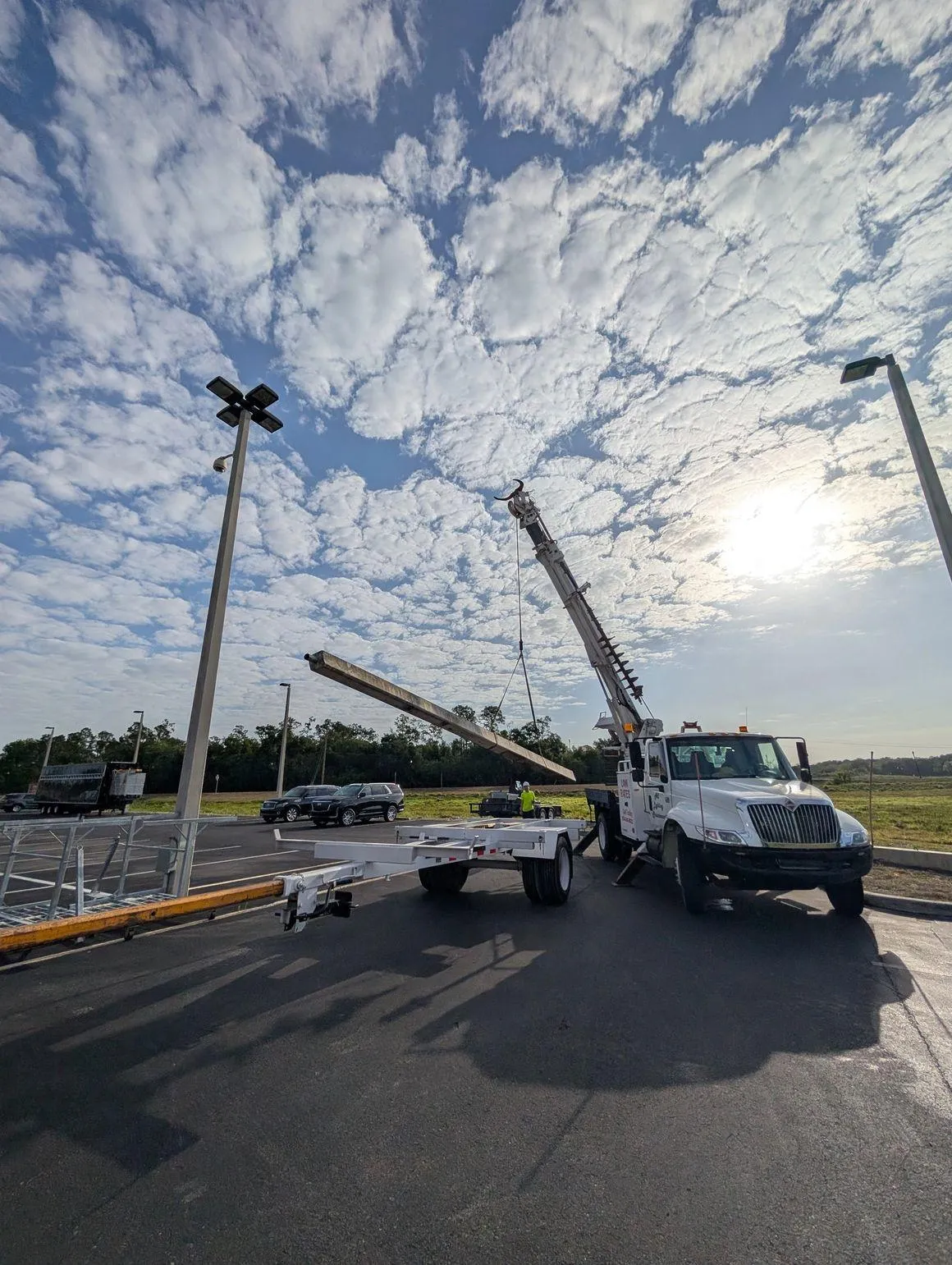 All Lighting Maintenance crane truck lifting a concrete light pole for installation in a commercial parking lot.