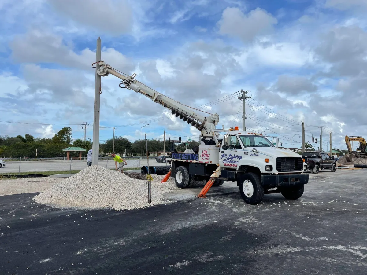 All Lighting Maintenance auger truck installing a concrete light pole at a new construction site in Florida.