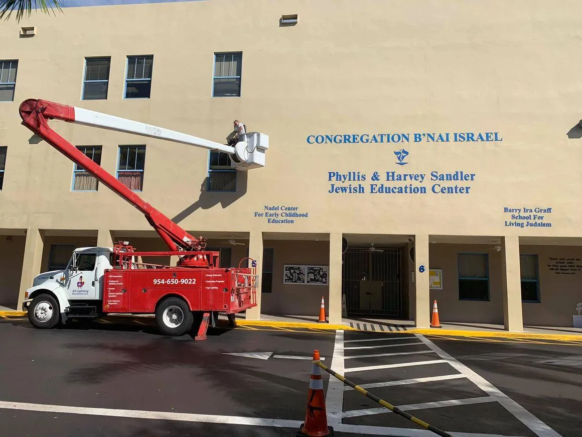 All Lighting Maintenance bucket truck performing building exterior lighting repairs at a school and community center.