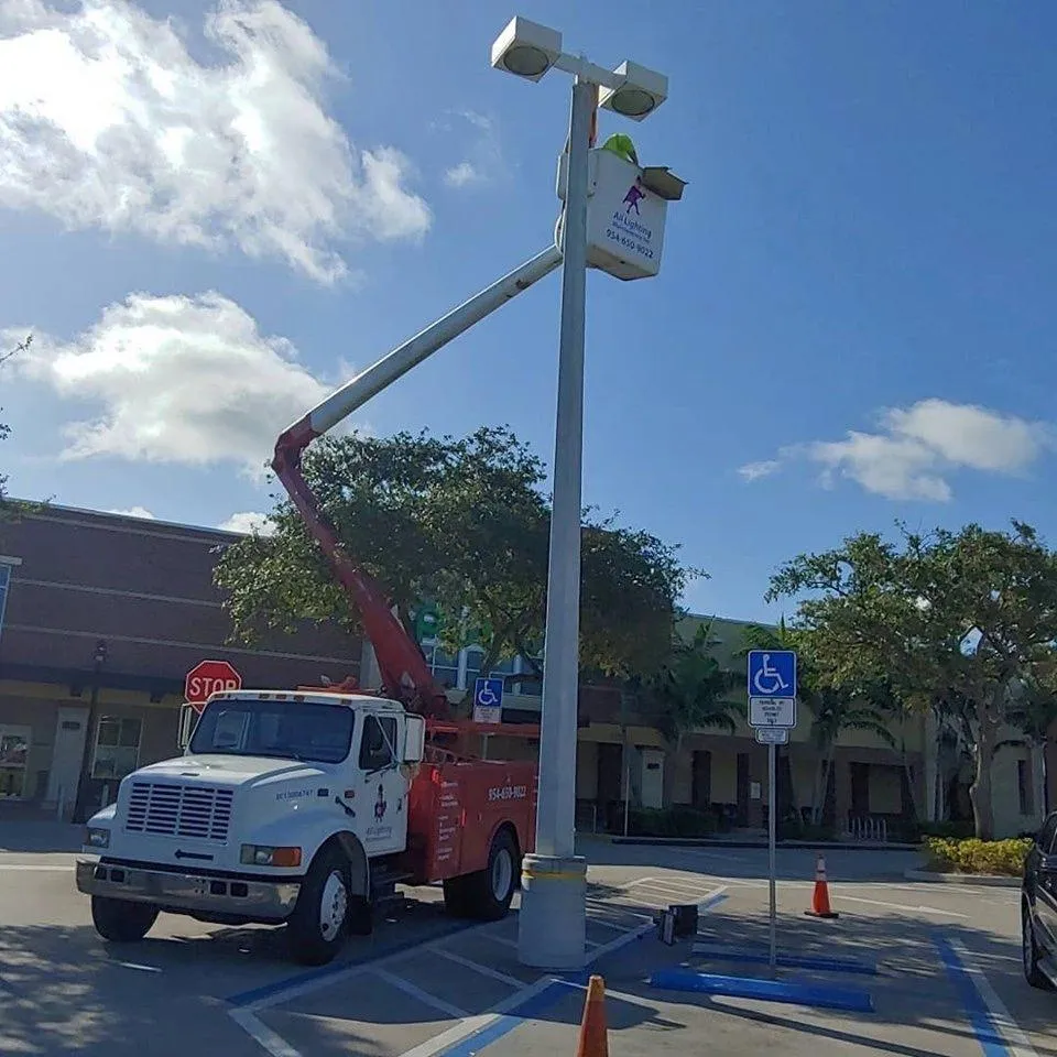 All Lighting Maintenance red bucket truck extended to repair a high-reach parking lot light.
