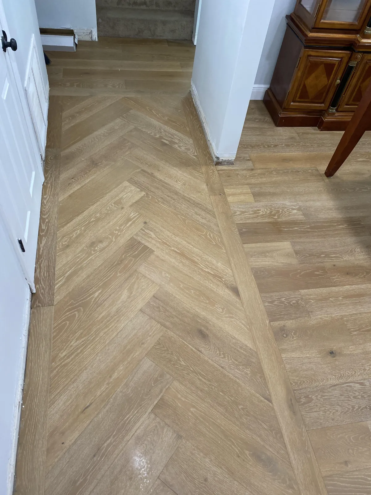Elegant hallway featuring light oak hardwood flooring in a herringbone pattern with a straight plank border.