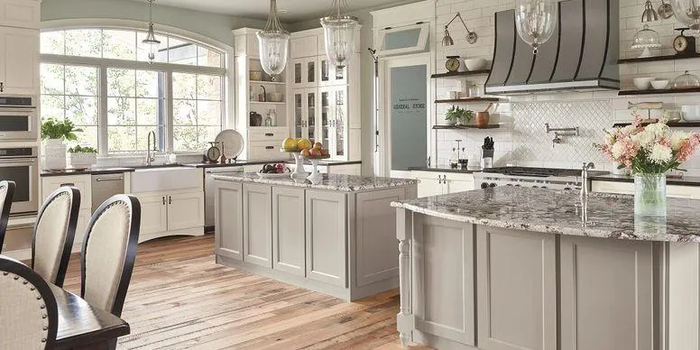 Luxury kitchen remodel featuring double grey islands, granite countertops, white perimeter cabinets, and rustic hardwood flooring.