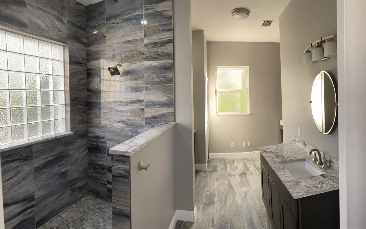 Master bathroom featuring a large walk-in shower with blue and grey marble-look porcelain tile, a glass block window, and matching stone-look flooring.