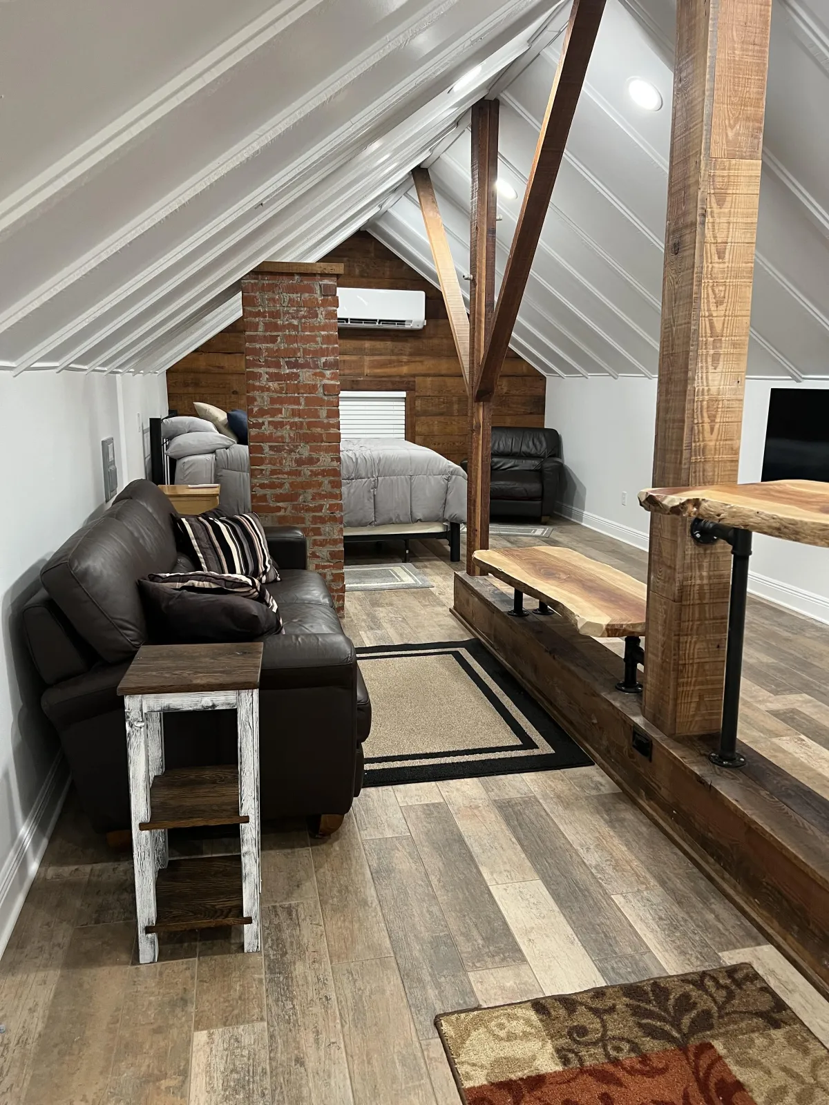 Rustic attic loft featuring wood-look plank flooring, exposed brick pillars, and custom live-edge wood shelving and bar counters.