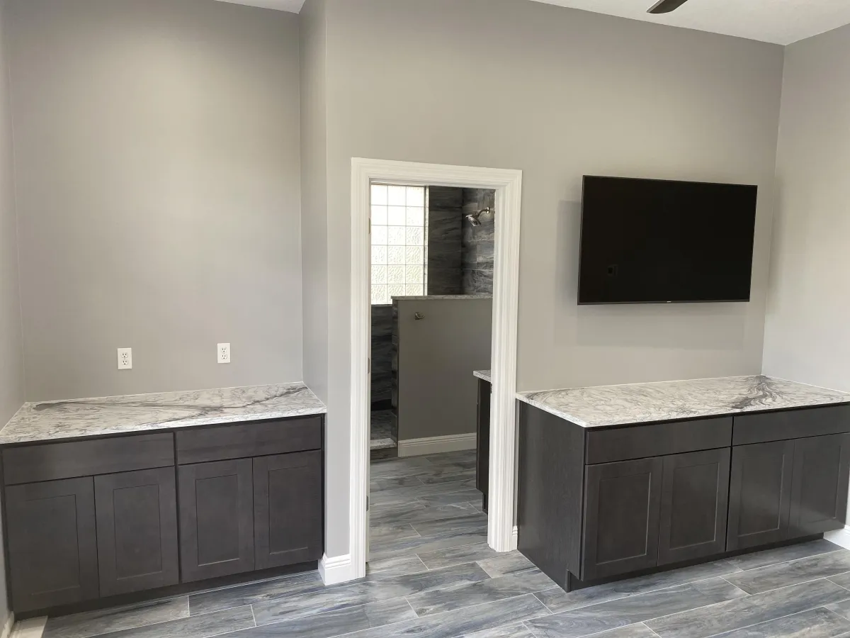 Modern bedroom featuring dark grey built-in base cabinets with white marble-look quartz countertops and grey wood-look plank flooring.