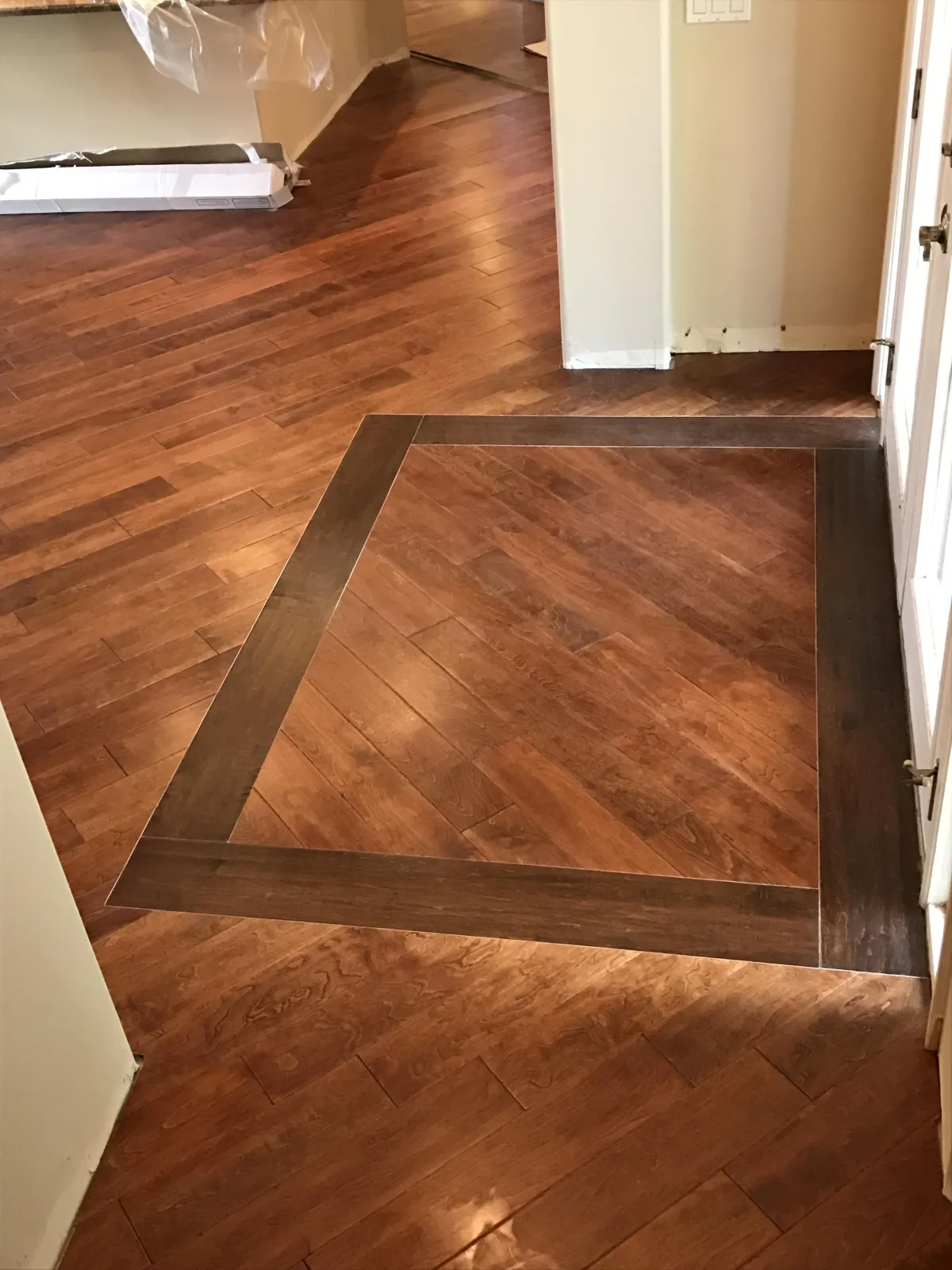 Close-up of a custom cherry hardwood floor installation featuring a dark walnut border inlay in an entryway.