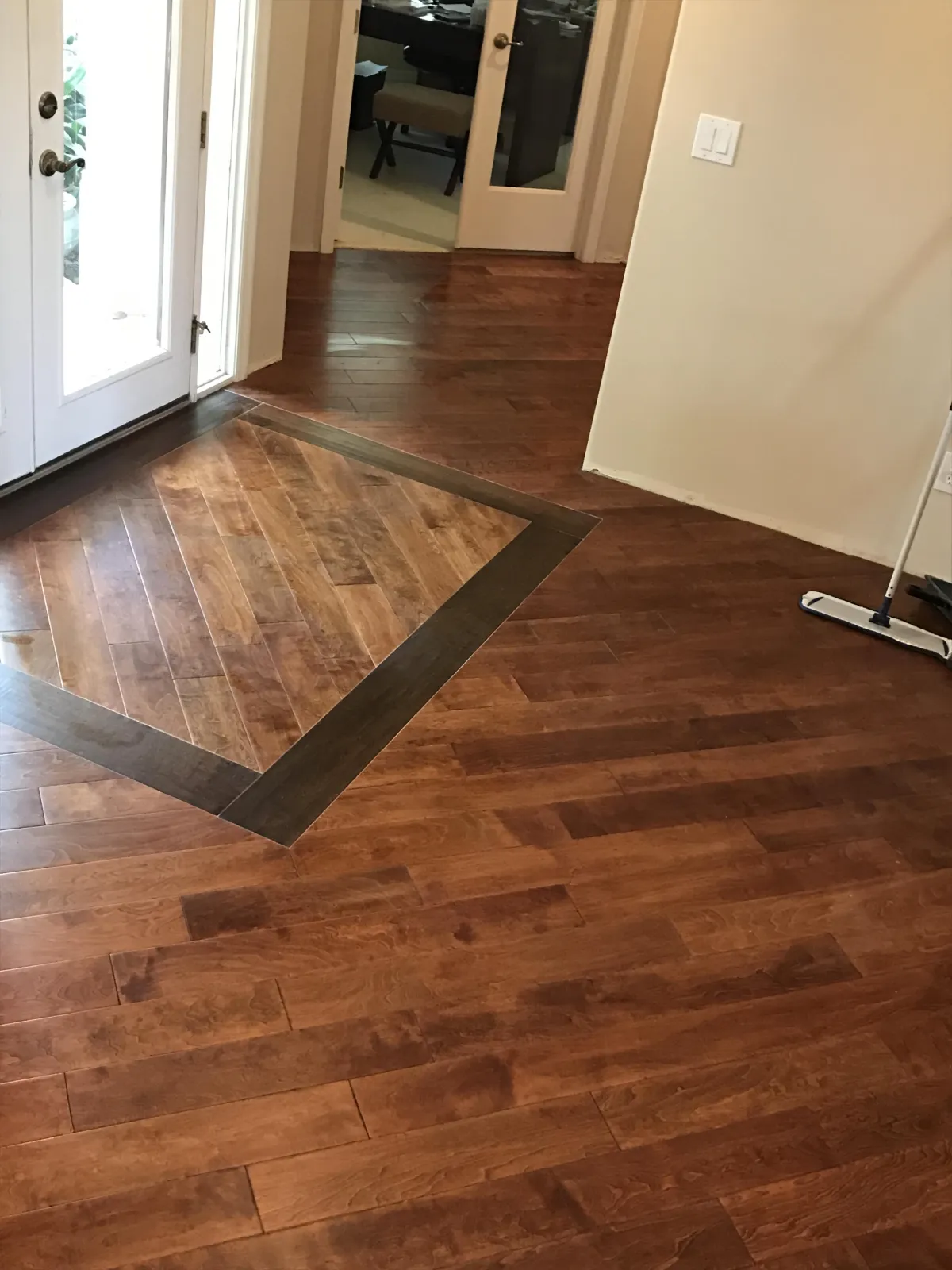 Foyer remodel featuring a custom square wood floor inlay with cherry planks and a dark walnut perimeter border.