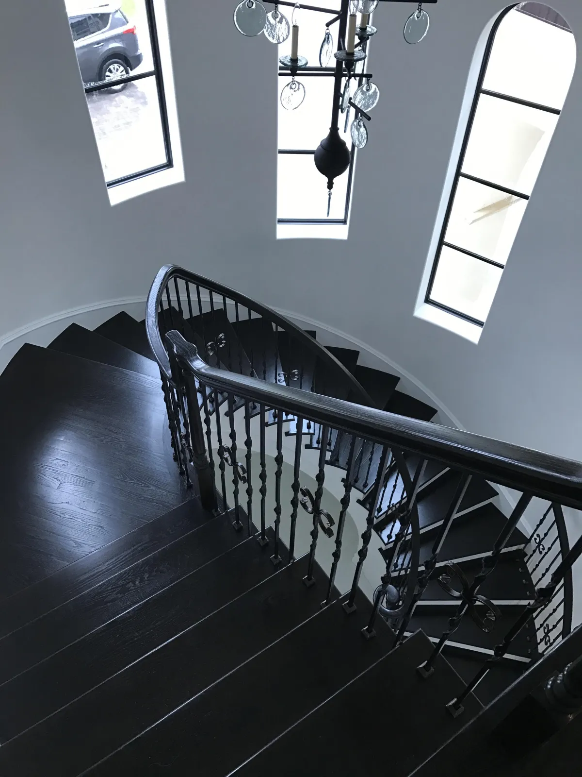 Elegant modern home interior showcasing a custom dark hardwood spiral staircase with intricate wrought-iron spindles. A unique glass chandelier hangs above the stairs.