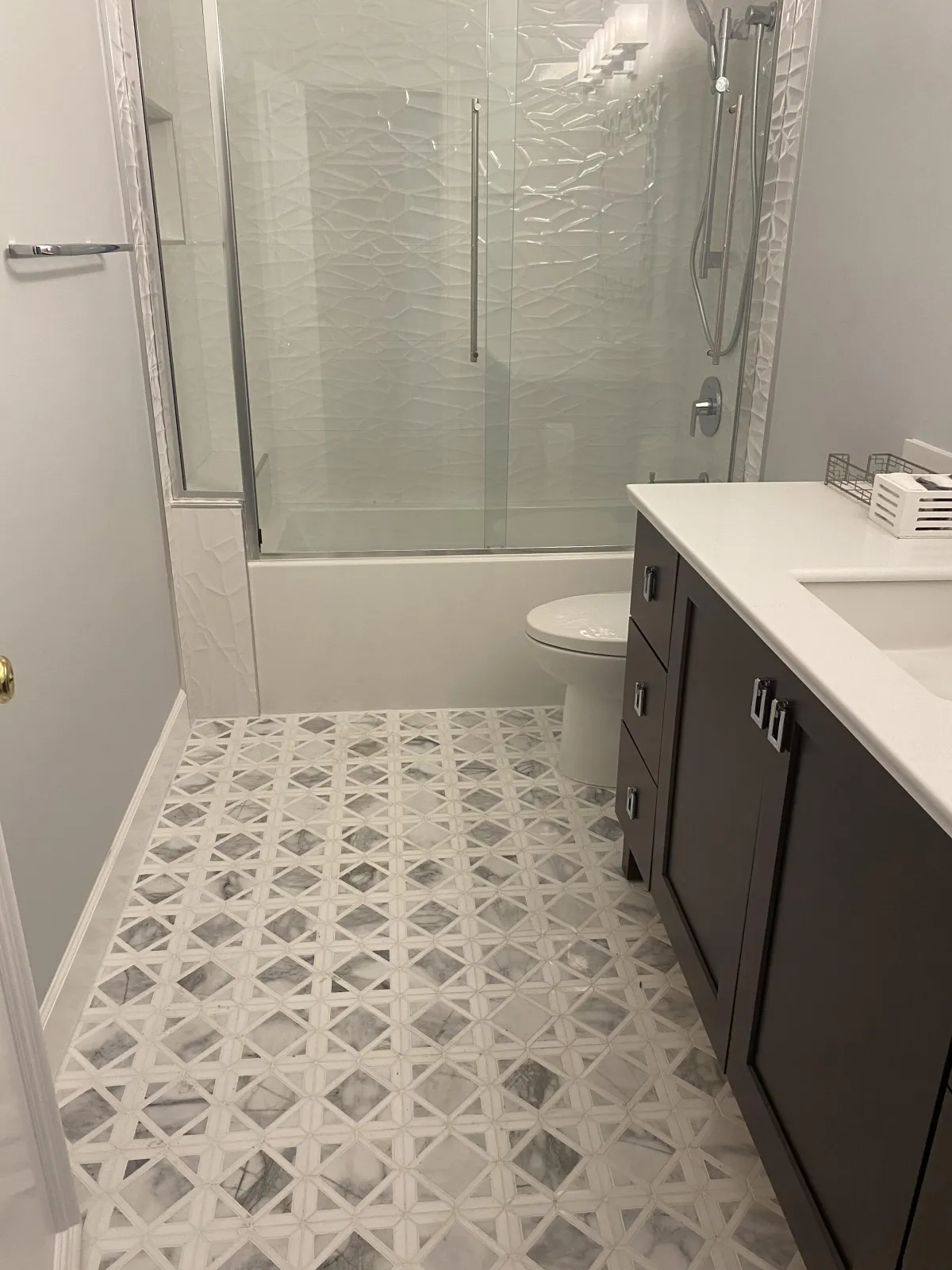Modern bathroom remodel featuring white and grey geometric marble floor tiles and a textured white 3D wall tile in the shower.