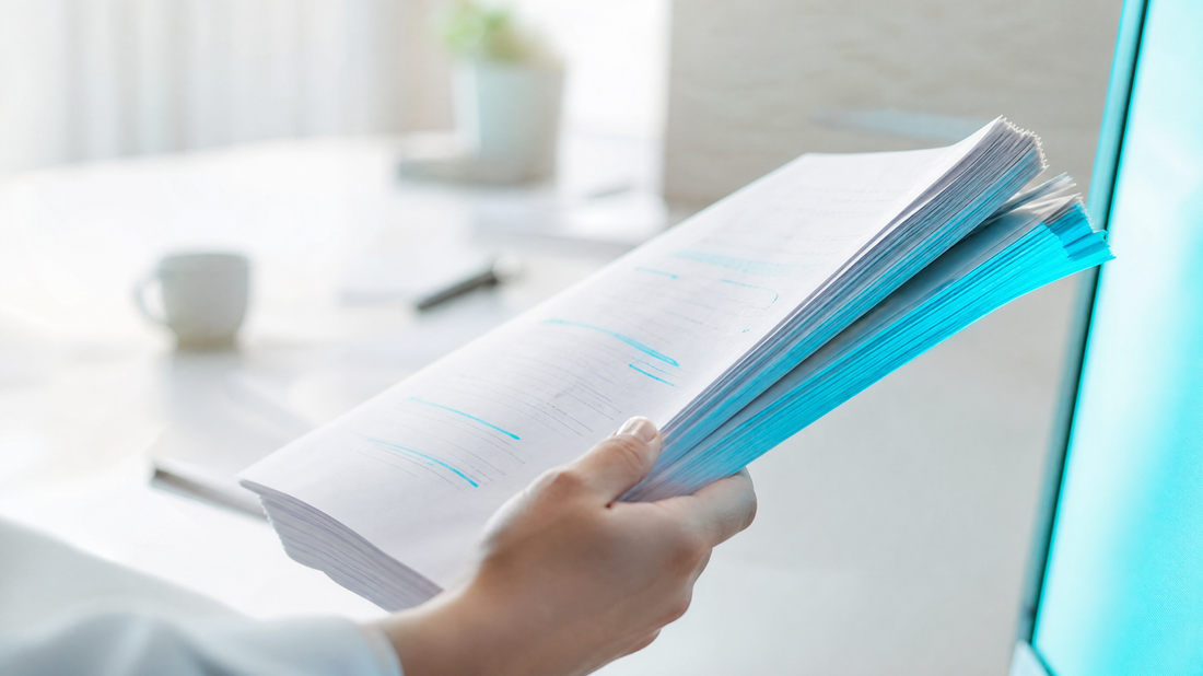 A hand holding a thick, marked-up report under cyan light.